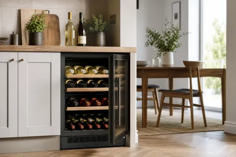 An under-counter wine fridge in a bright kitchen with mixed red and white wine bottles on shelves