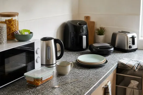 Microwave, kettle, toaster, air fryer and sandwich toaster arranged on a shared student kitchen worktop