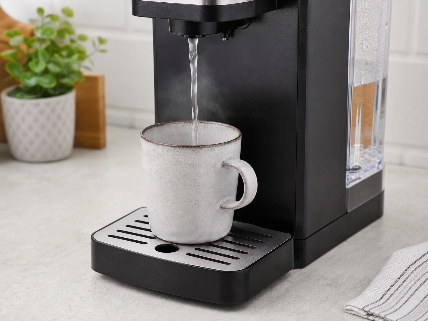 Hot water dispenser spout, mug, drip tray and side water tank on a kitchen worktop